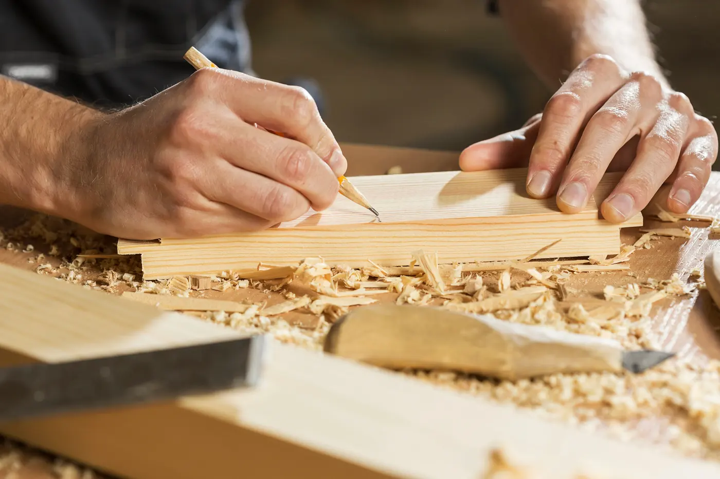 Mains d’artisan traçant une découpe sur une planche, entourées de copeaux